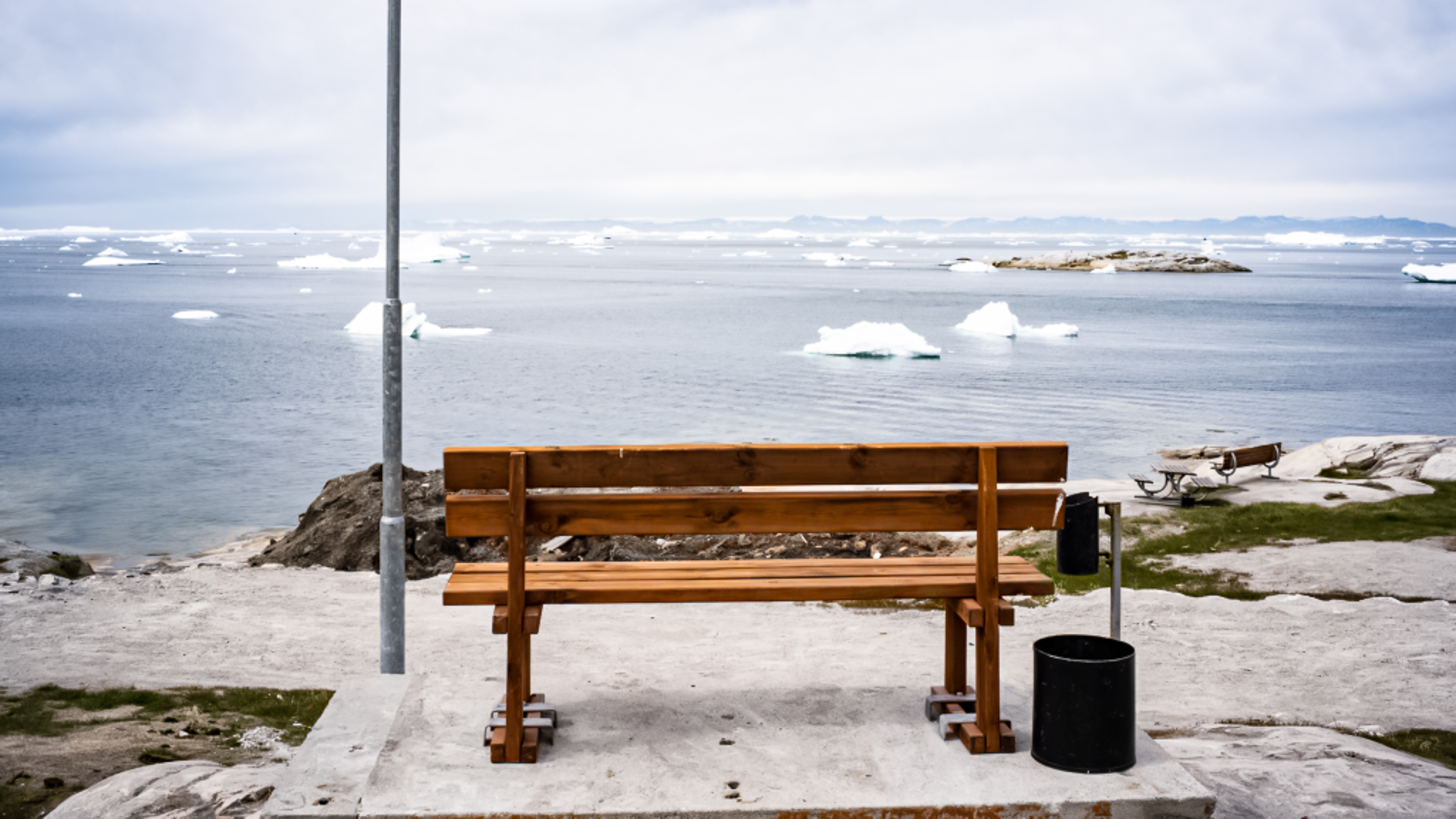 park bench overlooking arctic sea with icebergs, greenland