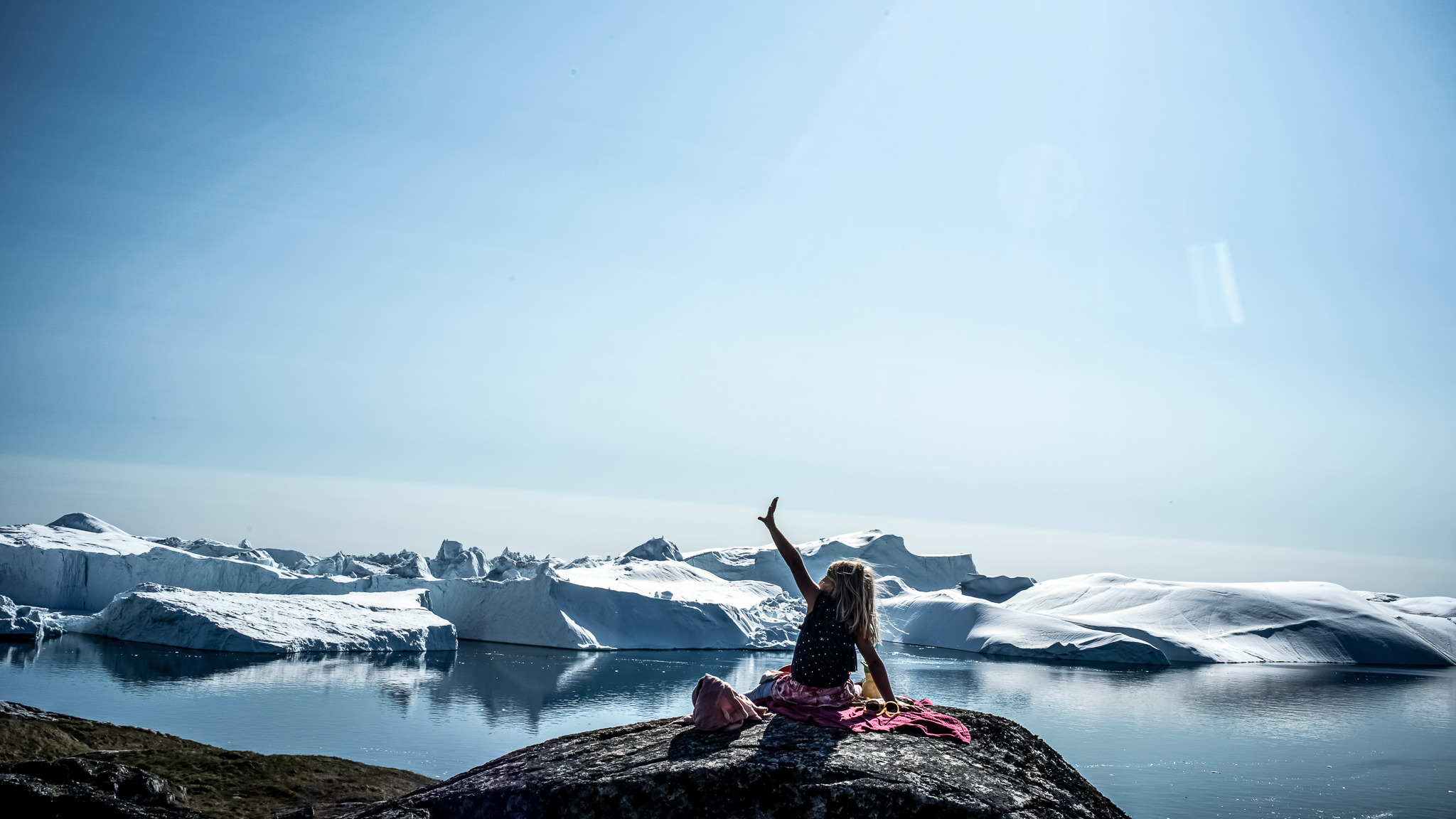 child on rock overlooking ilulissat icefjord, greenland